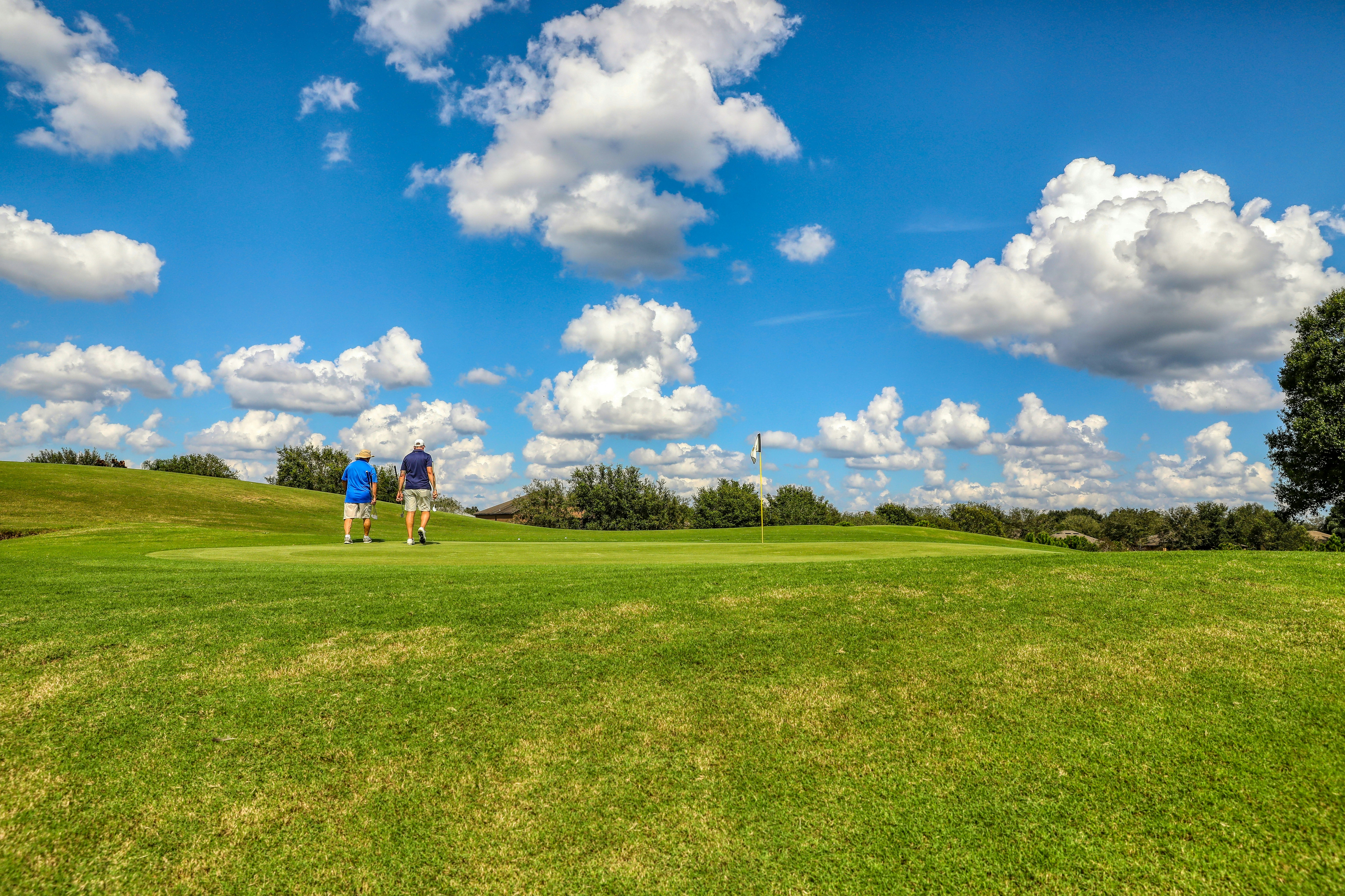 people playing golf on green grass field under blue and white cloudy sky during daytime